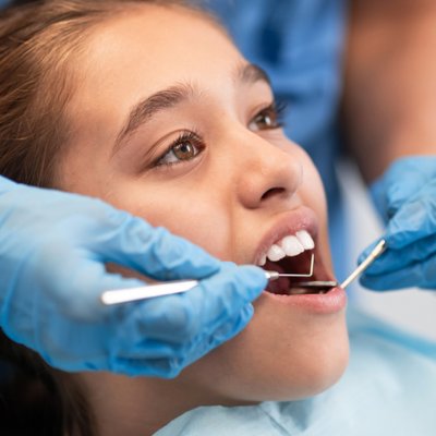 A young girl in close up as a dentist checks her teeth with instruments